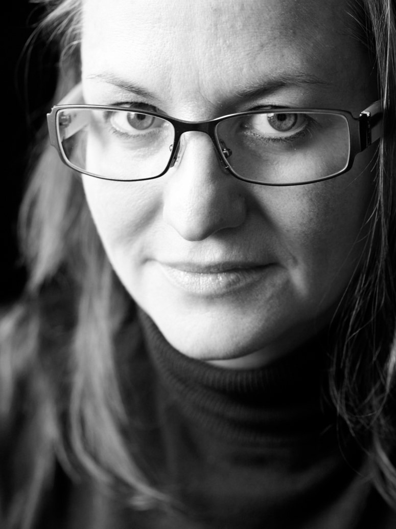 Portrait Celina Lunsford. Nahaufnahme Frau mit Brille vor schwarzem Hintergrund.