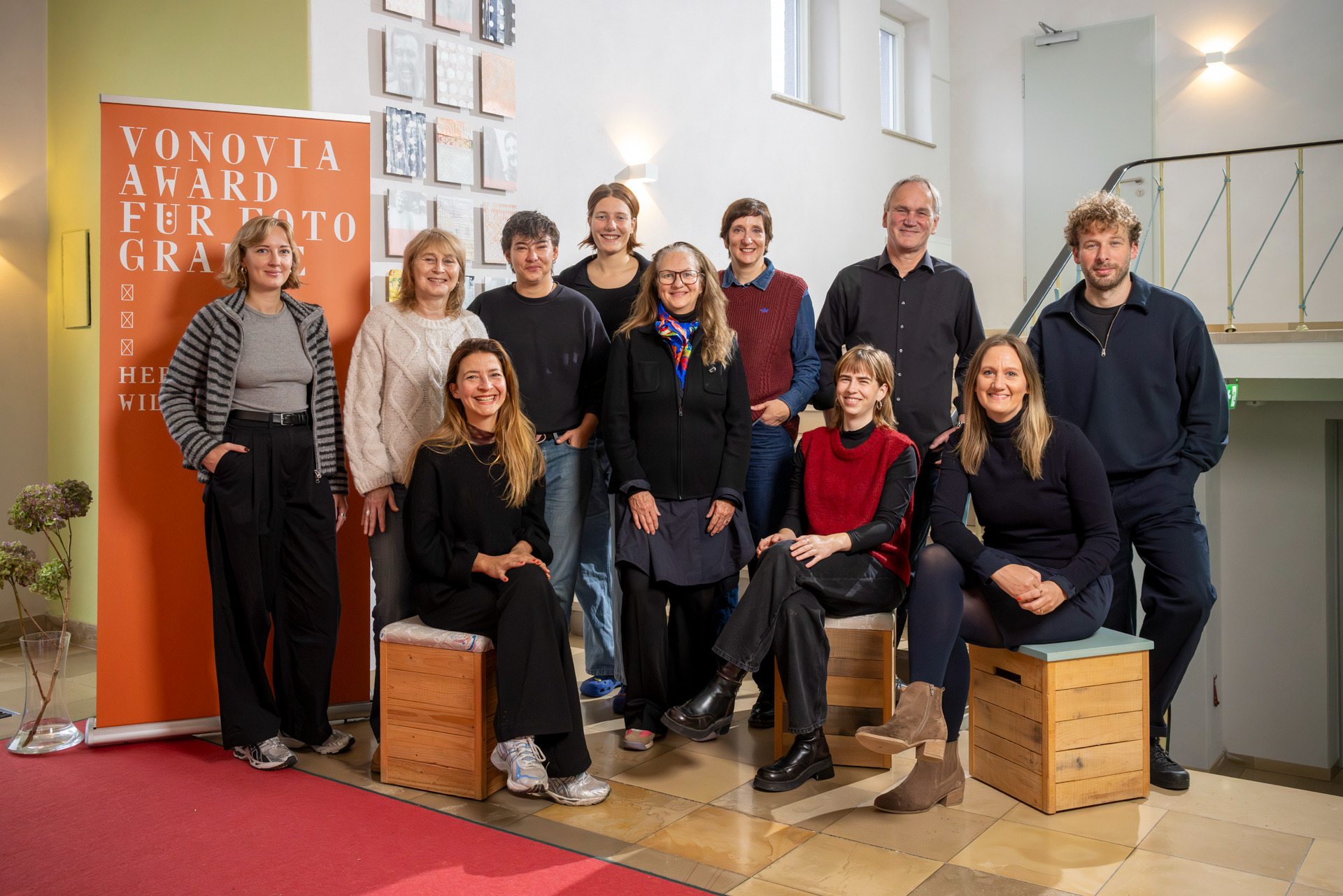 Eine Gruppe von 11 Personen steht und sitzt in einem Innenraum vor einem Banner für den Vonovia Award für Fotografie.