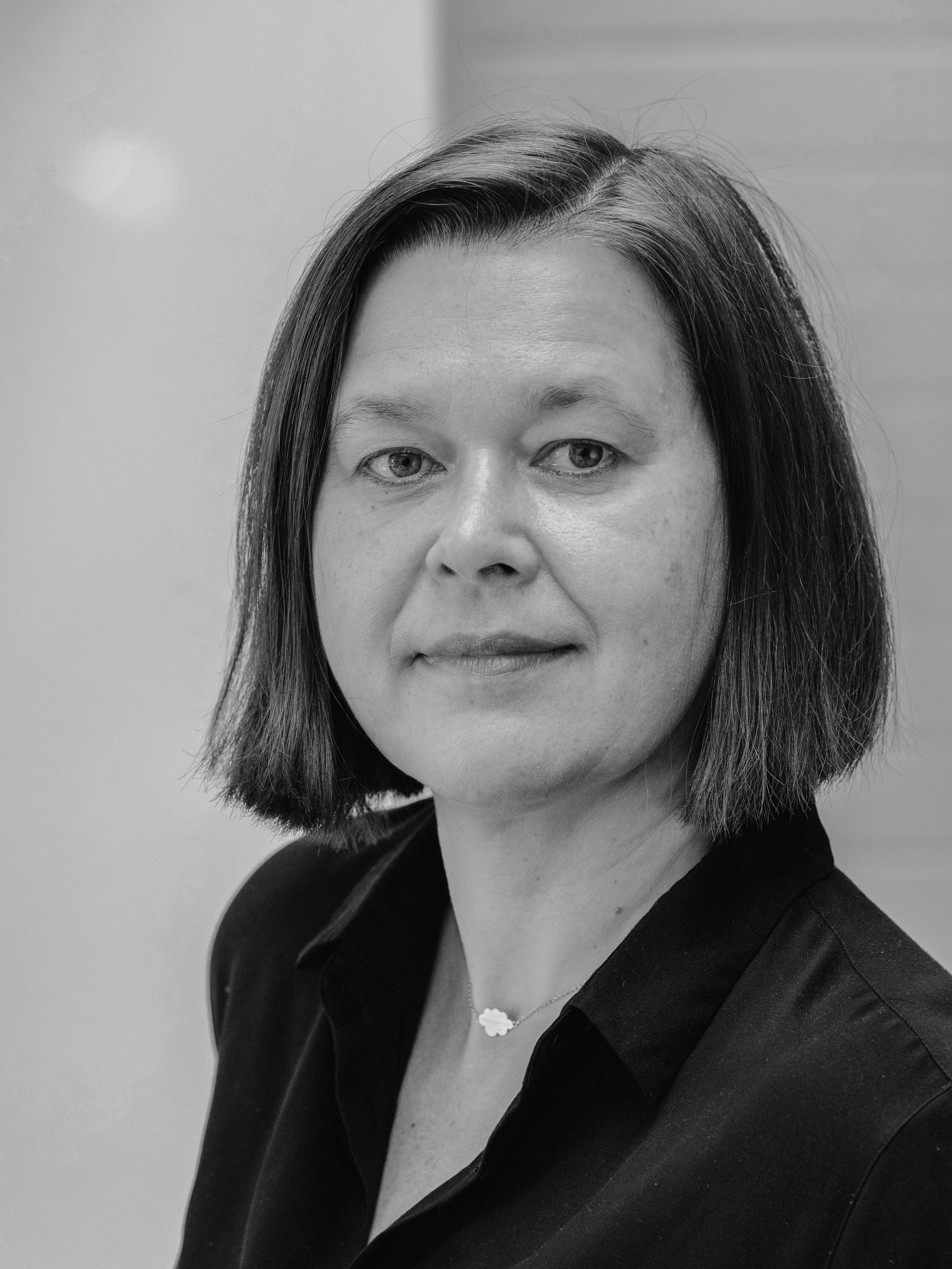 Schwarz weiß Portrait Silke Frigge. Frau in dunklem Hemd vor neutraler Wand.