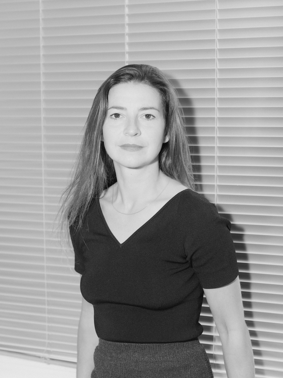 Schwarz weiß Portrait Paula Markert. Frau in dunklem T-Shirt steht vor Rollladen.