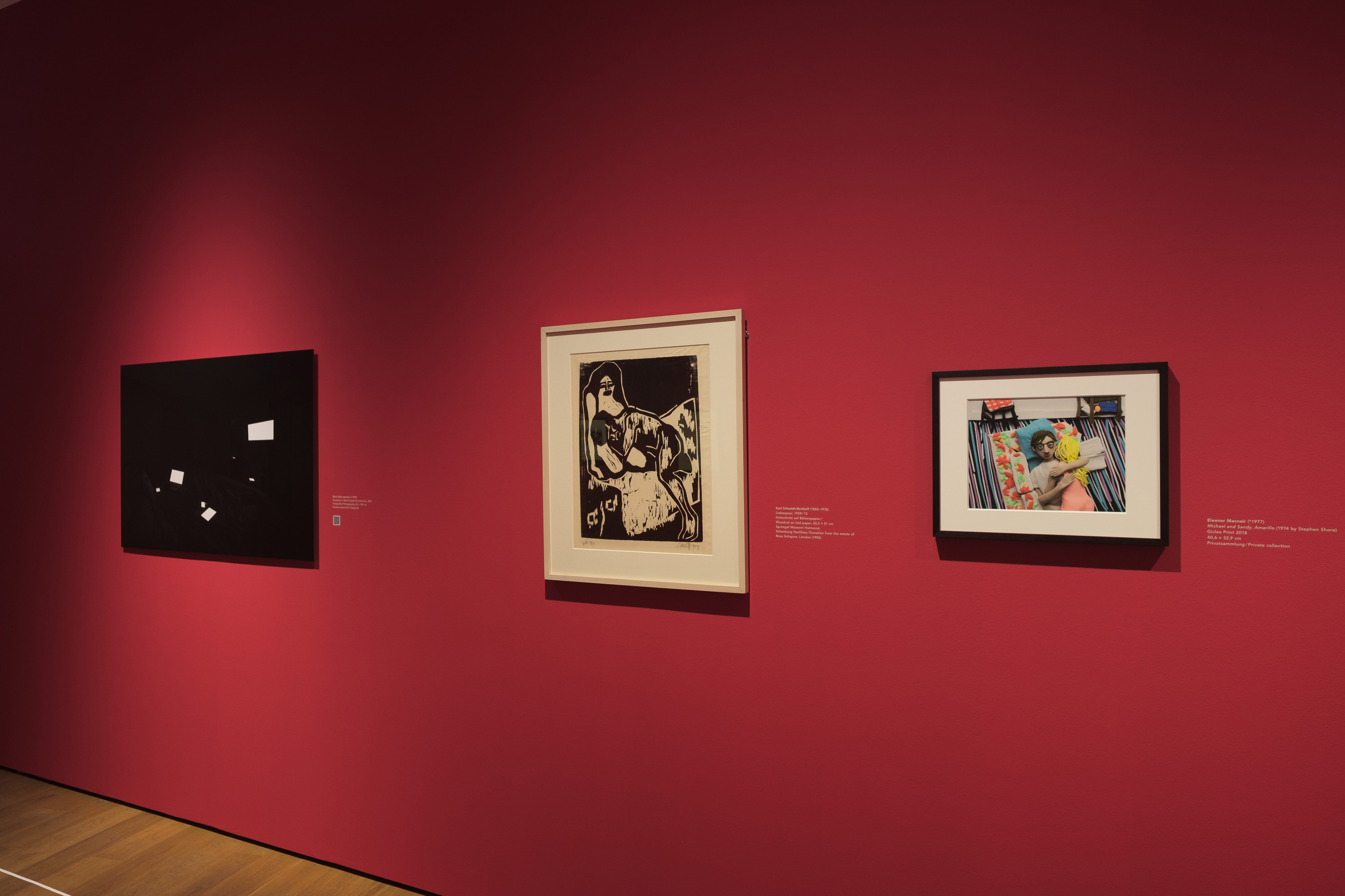 Drei Fotografien, eingerahmt, an einer roten Wand.